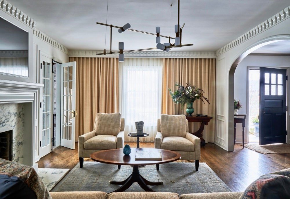 Living room with wall to wall cream curtains, upholstered armchairs and round pedestal table, by Martire Custom Homes