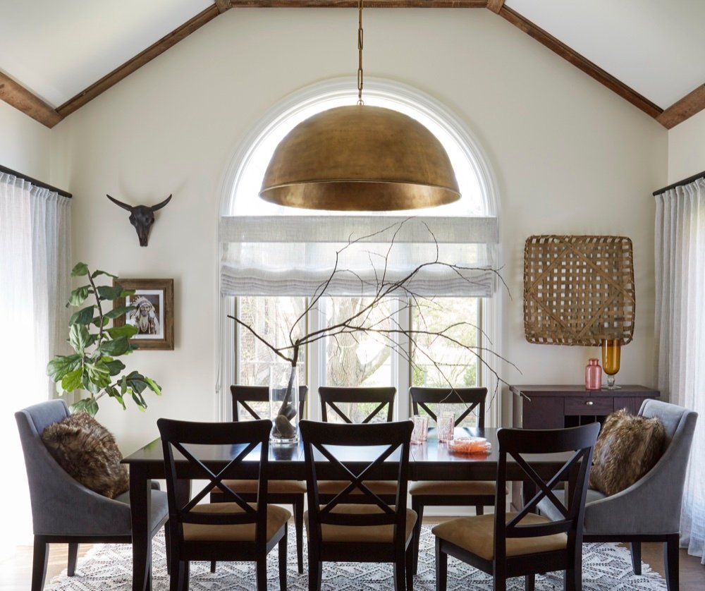 Vaulted dinette with reclaimed wood beam trim, an oversized aged-brass dome pendant, arched window and dark dining table with cross-back chairs, by Martire Custom Homes
