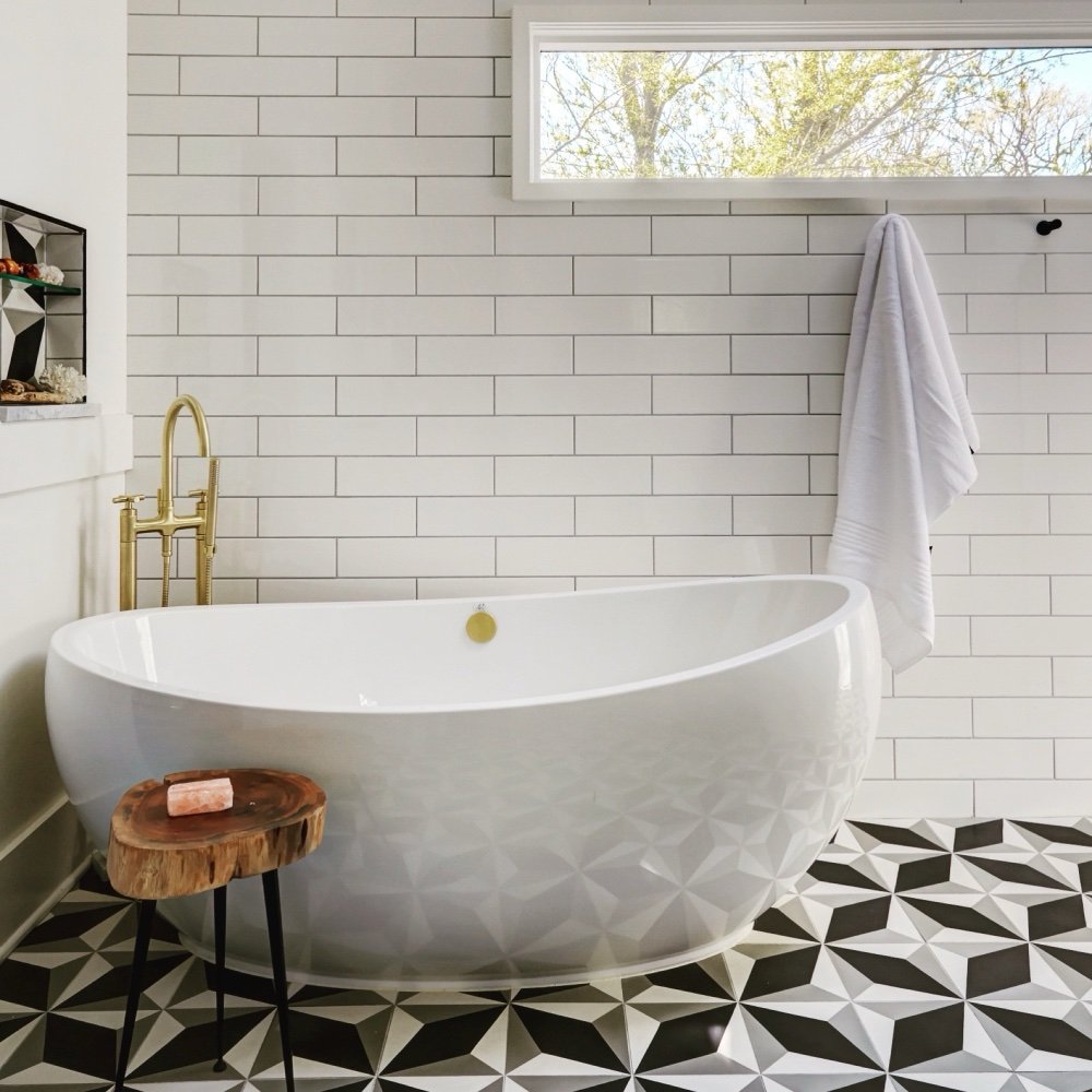 Freestanding sculptural tub with a faceted base, brass floor-mounted filler, white subway tile and geometric cement tile floor in the primary ensuite, by Martire Custom Homes