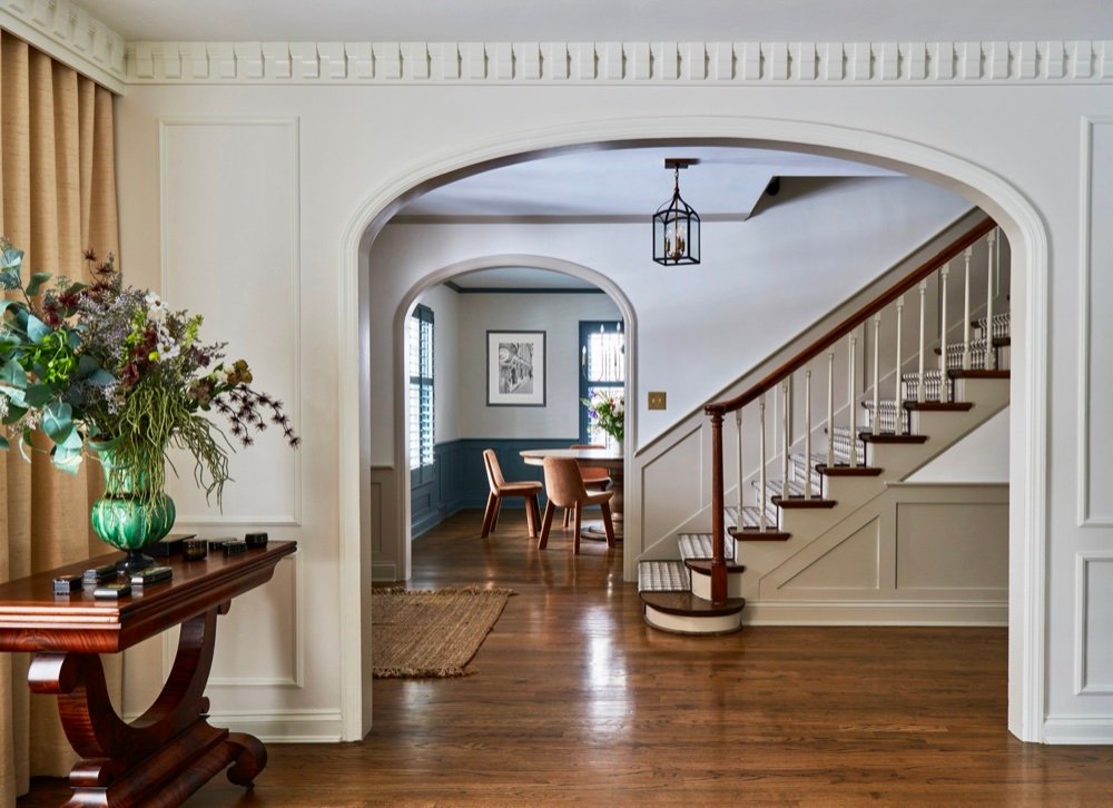 Arched foyer and stair hall with dentil crown molding, a mahogany console with wildflowers, and a houndstooth-runner staircase, renovated by Martire Custom Homes