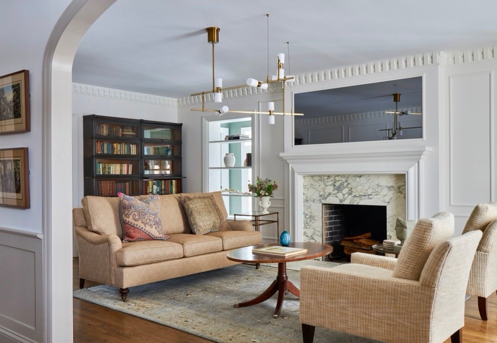 Living room with glass-front barrister bookcases filled with vintage books, wheat linen sofa, and marble fireplace, by Martire Custom Homes