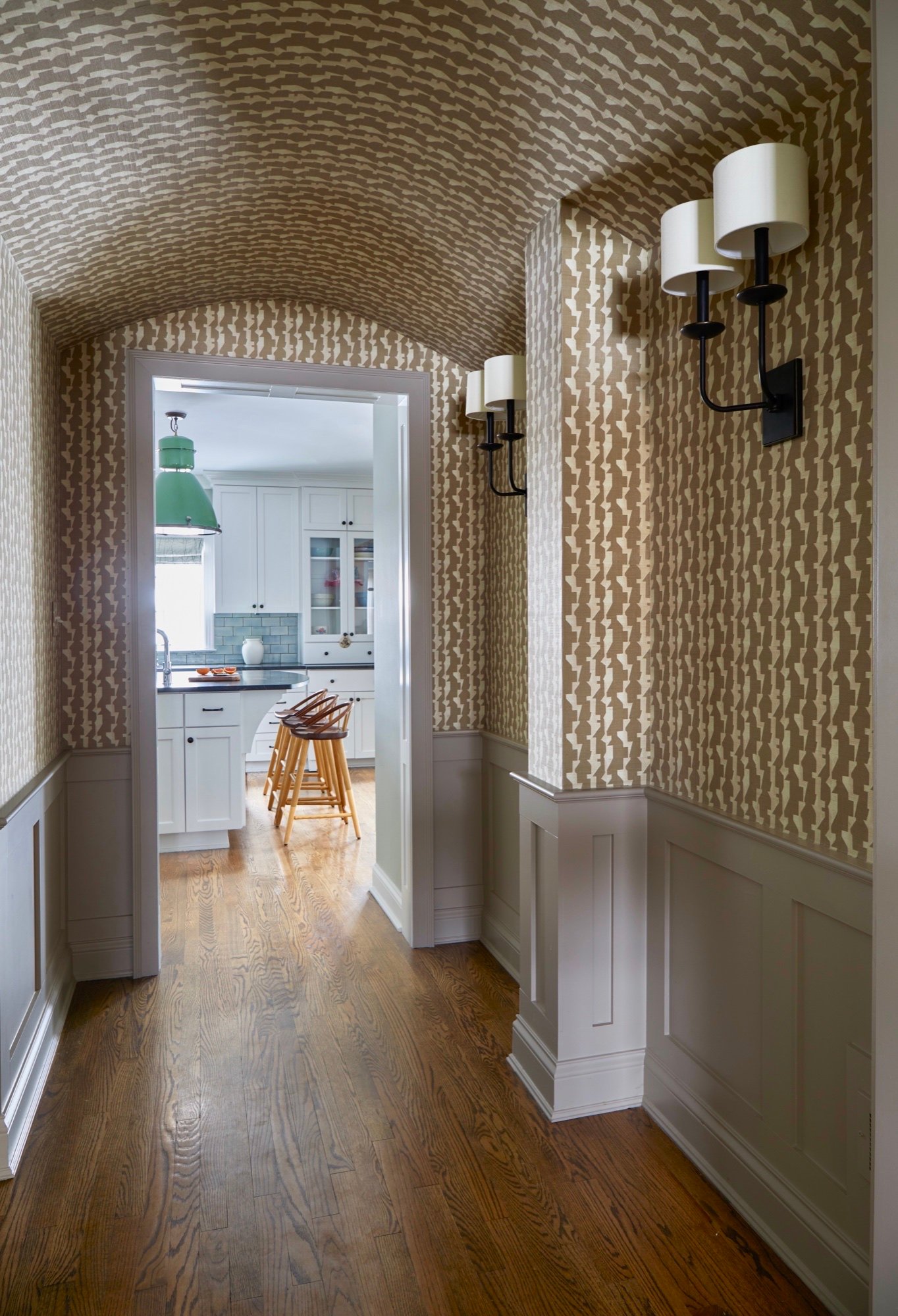Wallpapered barrel-vault hallway opening to the kitchen, where a vintage green shop lantern hangs above the island, by Martire Custom Homes