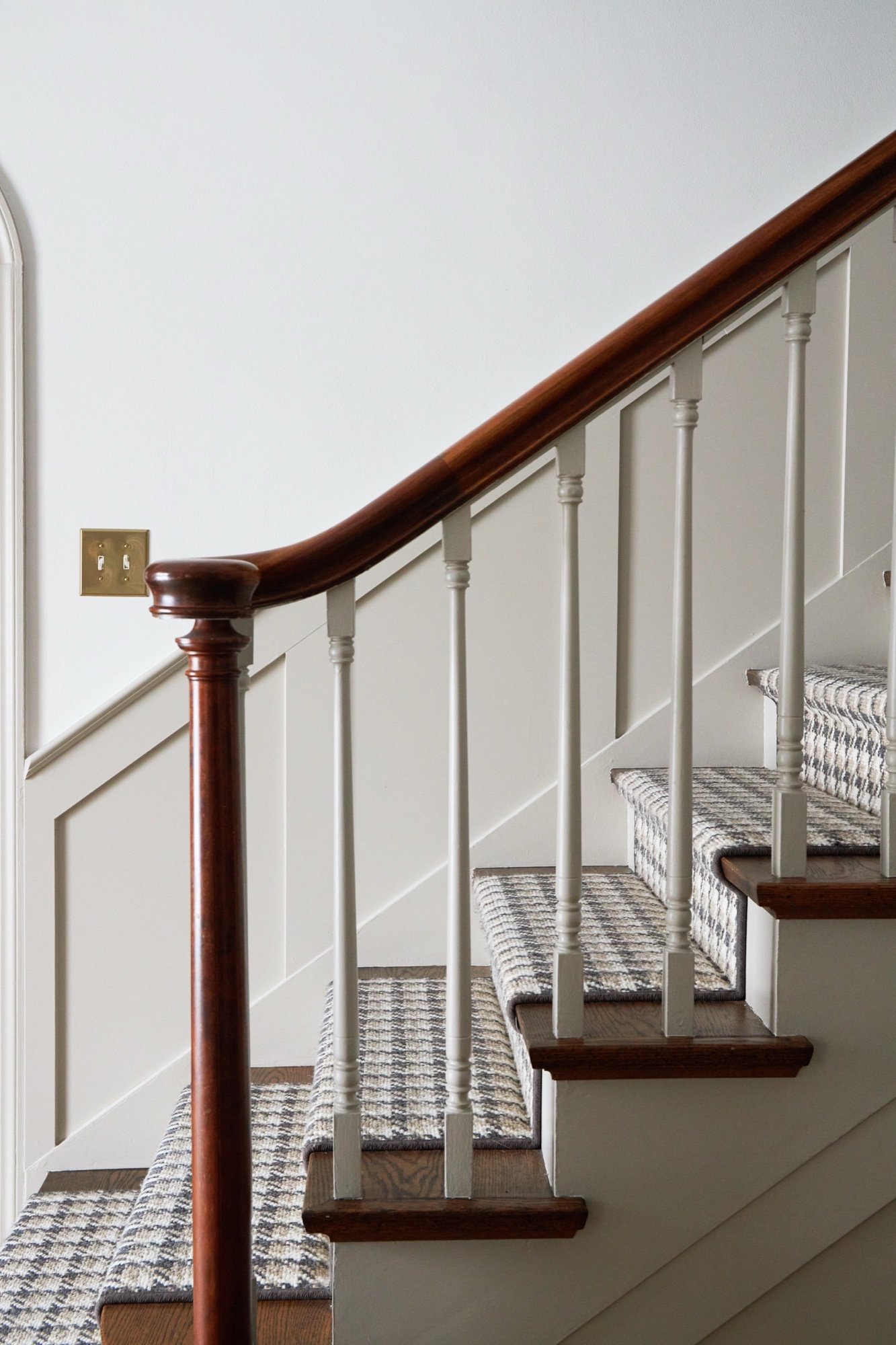 Staircase detail of curved mahogany handrail, painted spindles, paneled wainscoting, and checked wool stair runner, by Martire Custom Homes