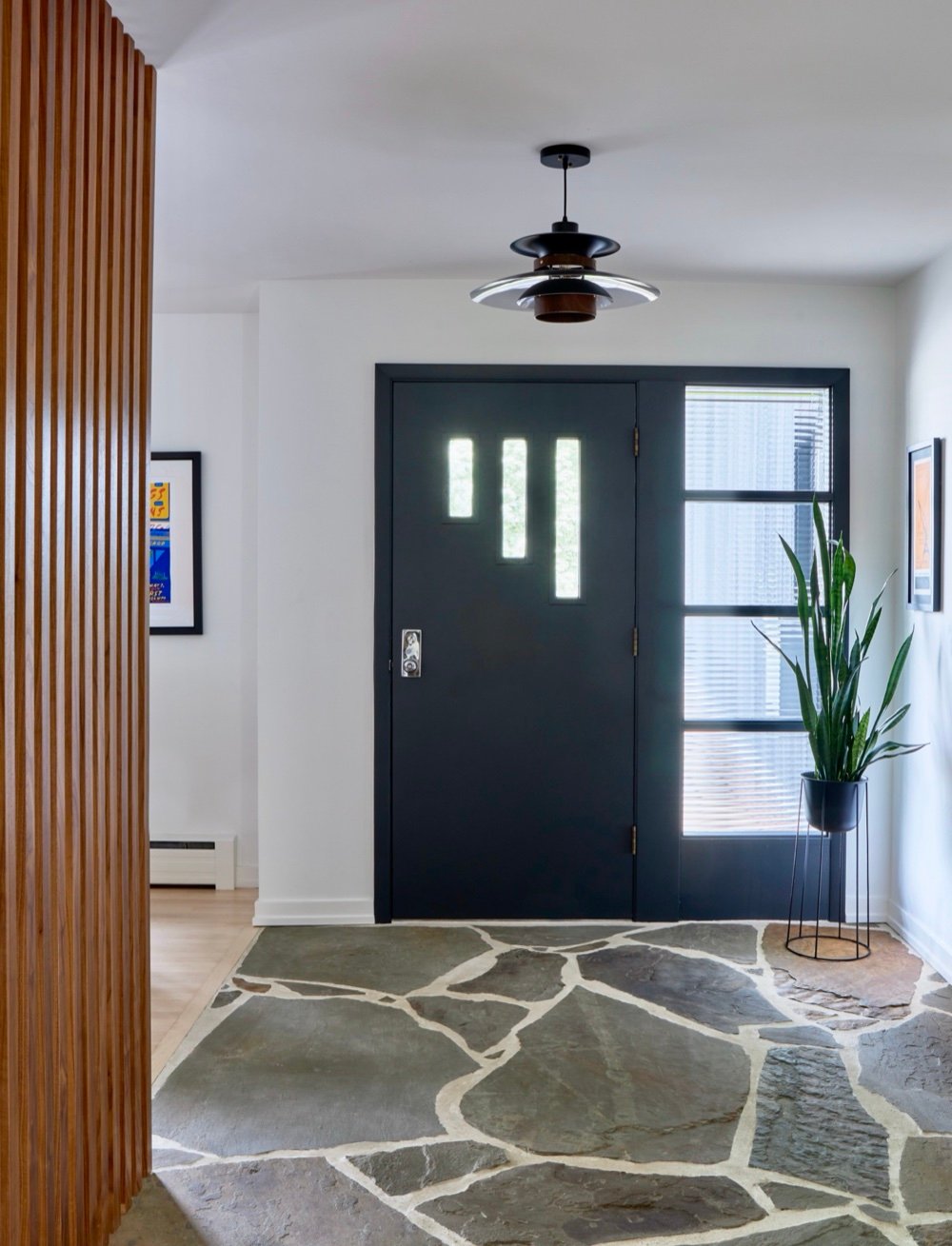 Mid-century modern foyer with a charcoal entry door and sidelight, natural flagstone floor, walnut slat wall and period pendant by Martire Custom Homes