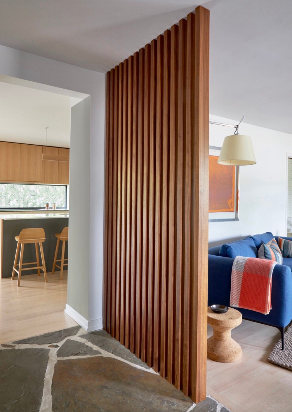 Floor-to-ceiling walnut slat trim wall dividing the flagstone foyer from the living room, with the kitchen island visible beyond, by Martire Custom Homes