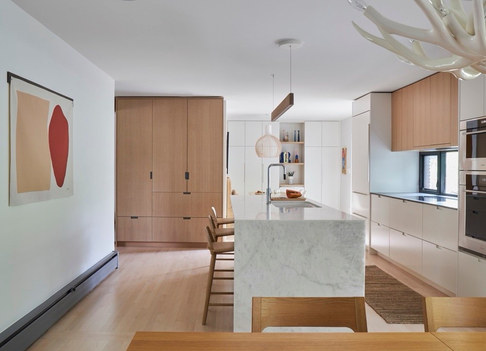 Open kitchen with marble waterfall island, floor-to-ceiling white cabinetry, white oak wardrobe wall and sculptural wood pendants by Martire Custom Homes