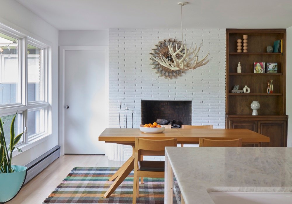 Mid-century dining room with white painted brick fireplace, sculptural antler chandelier, oak dining table, plaid rug and original walnut built-in shelving by Martire Custom Homes