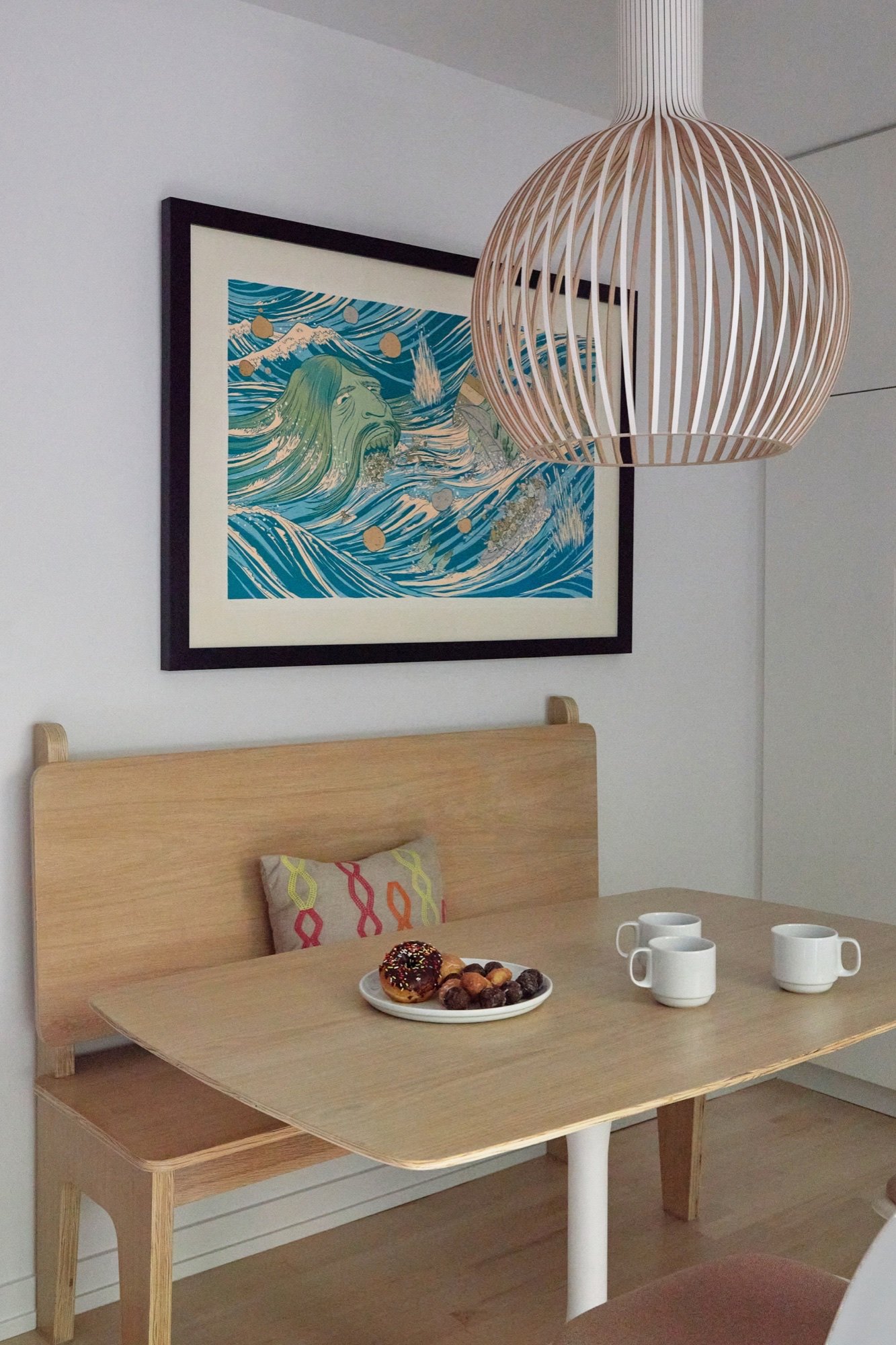 Breakfast dinette with a built-in plywood bench, oak table, sculptural slatted birch pendant and framed wave print by Martire Custom Homes