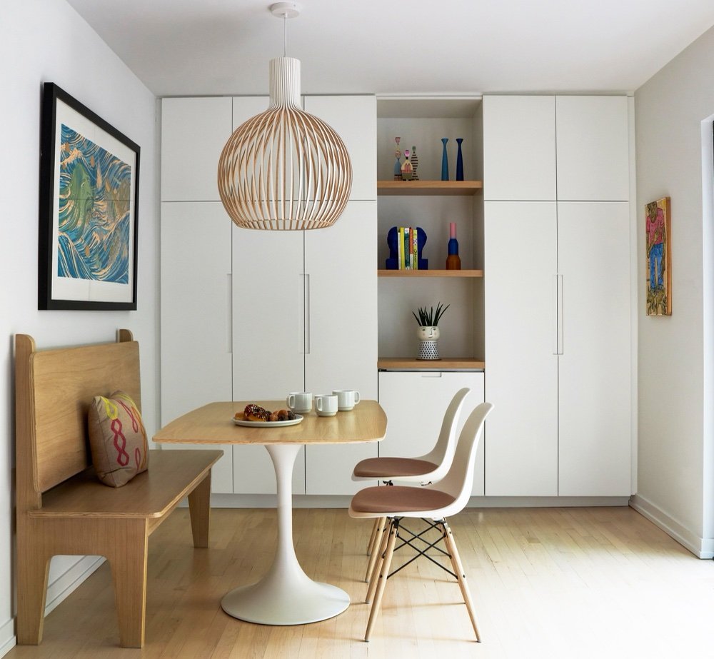 Dinette with white pedestal table, molded side chairs, plywood bench and a wall of white built-in cabinetry with an open display niche by Martire Custom Homes