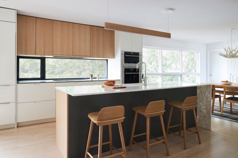 Scandinavian-inspired kitchen with rift white oak upper cabinets, ribbon backsplash window, marble-topped island with charcoal base and oak stools by Martire Custom Homes