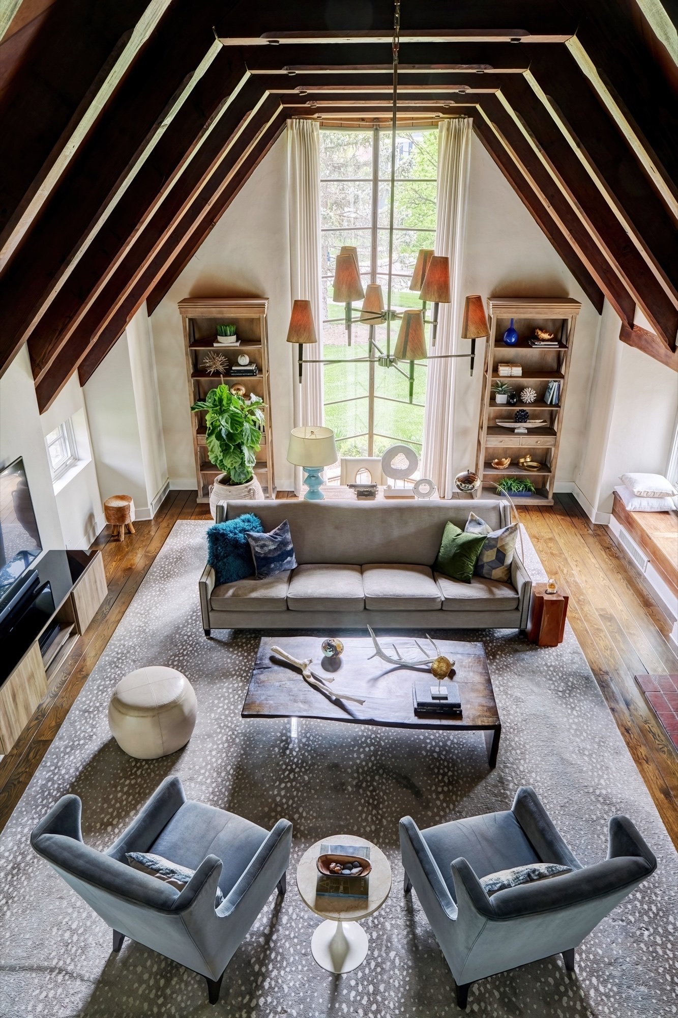 Vaulted great room seen from the loft, with restored wood plank ceiling, exposed rafters and a full-height V-mullioned window, by Martire Custom Homes