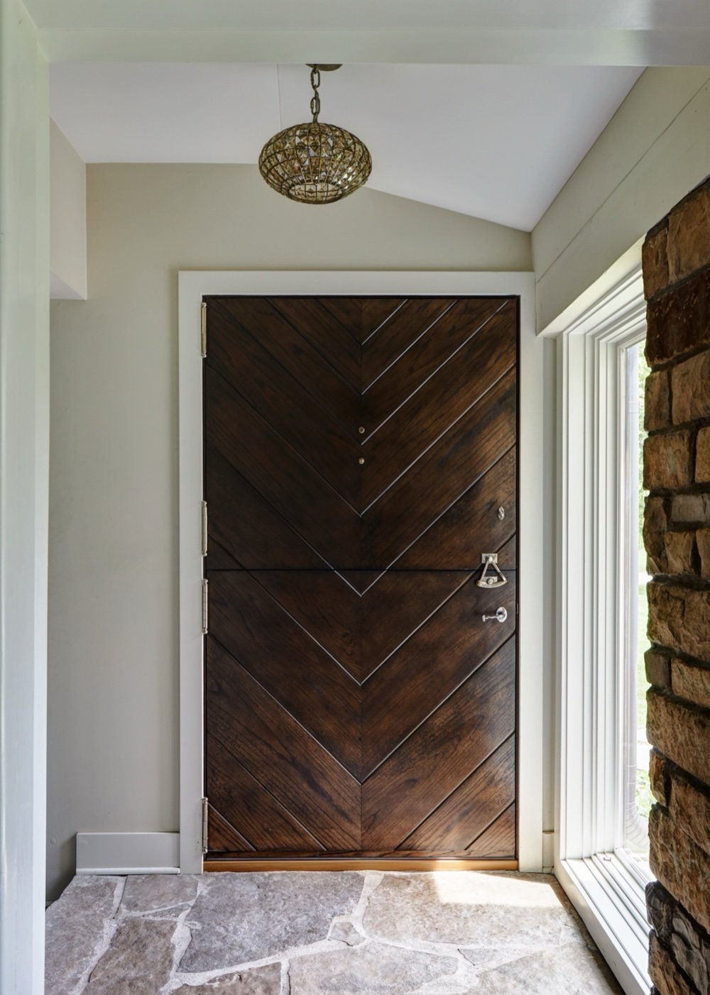 Chevron-paneled Dutch front door in dark-stained oak with nickel hardware, flagstone floor and original stone wall at the entry, by Martire Custom Homes