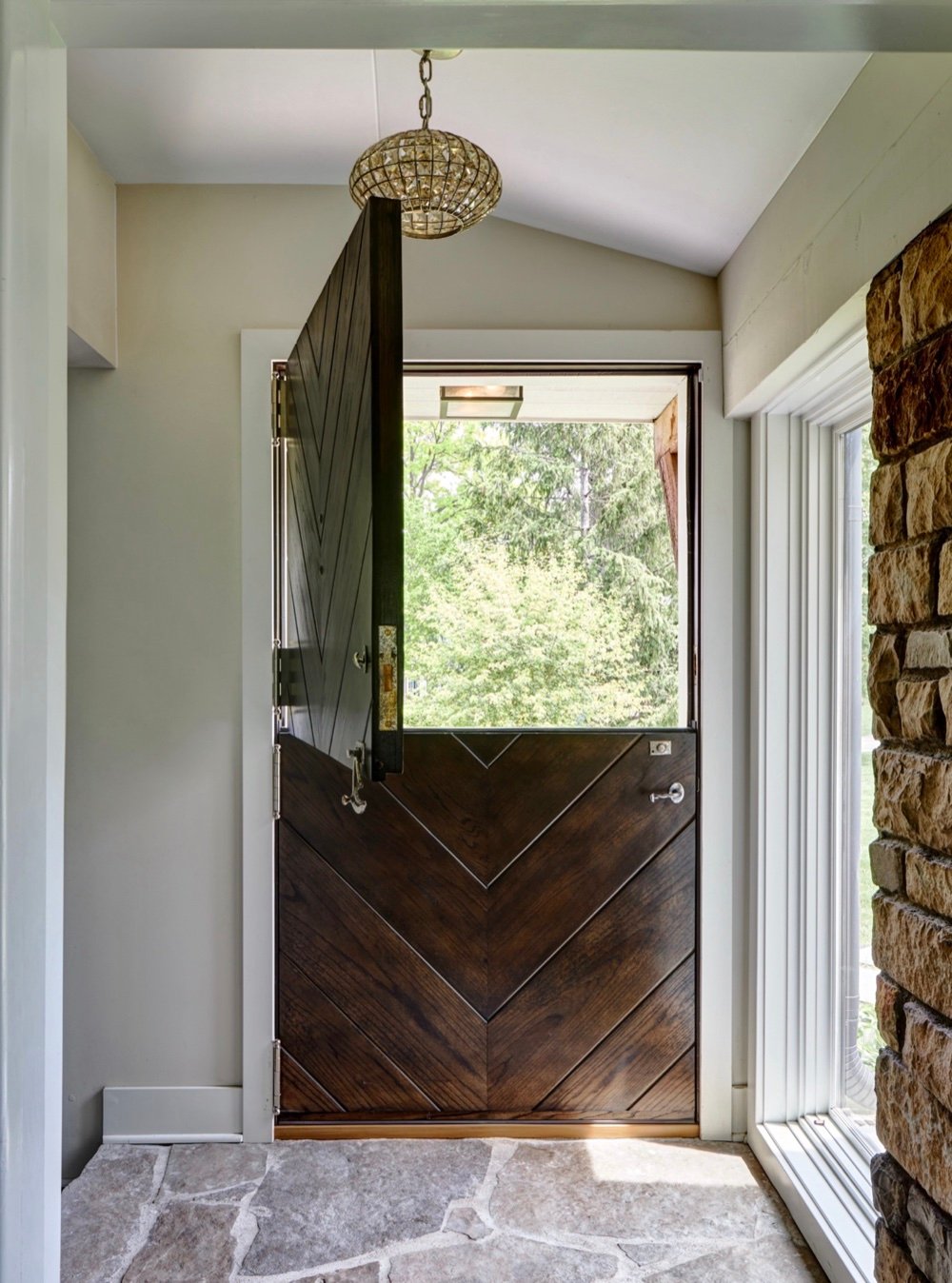 Restored Dutch front entry door with its upper leaf swung open to the trees, chevron oak paneling and flagstone entry floor, by Martire Custom Homes