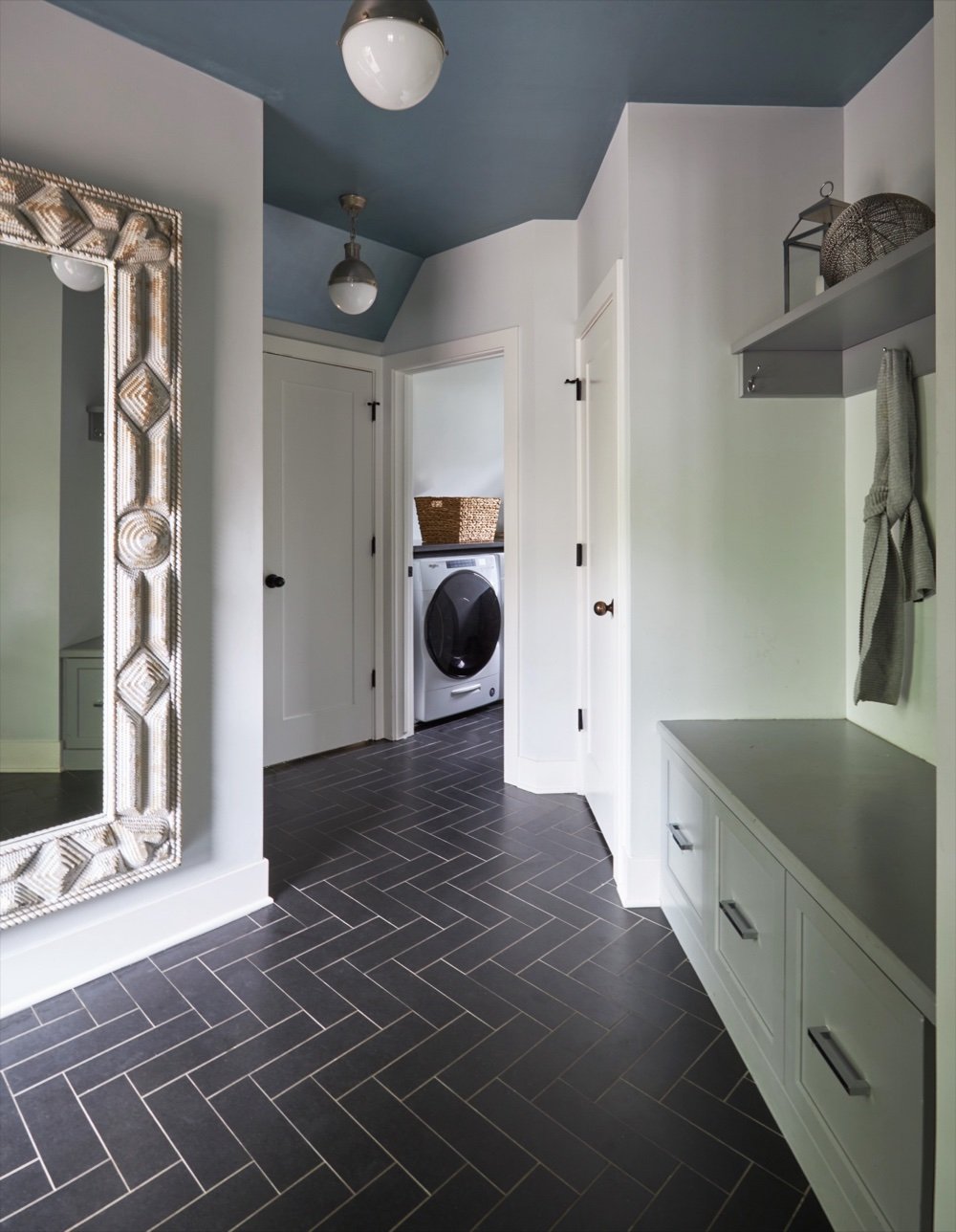 Storybook mudroom with black slate herringbone tile floor, globe pendants, gray bench cabinetry and silver leafed mirror, by Martire Custom Homes