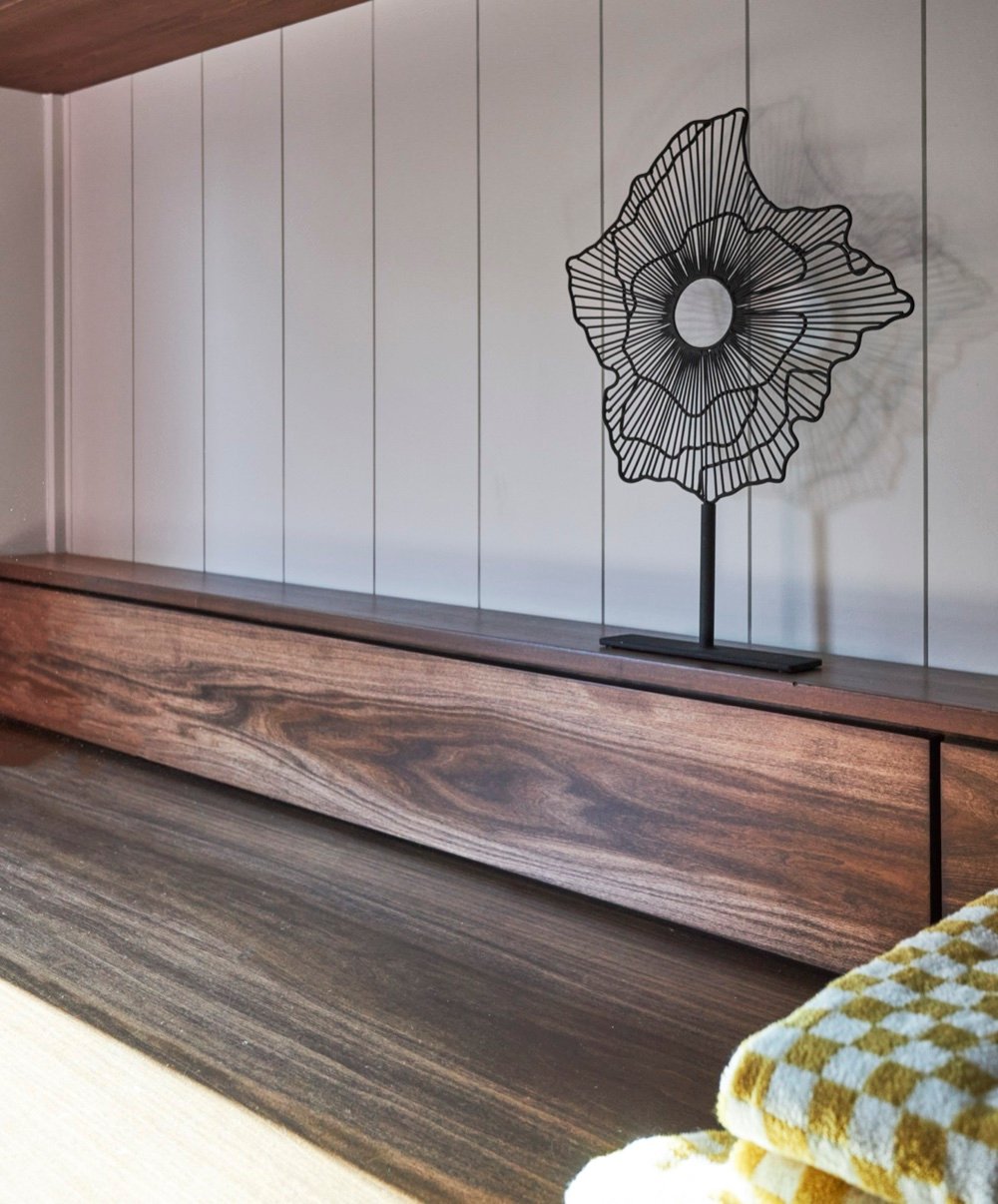 Custom walnut folding counter in the laundry room shown closed, set against vertical shiplap panelling with a wire sculpture, by Martire Custom Homes