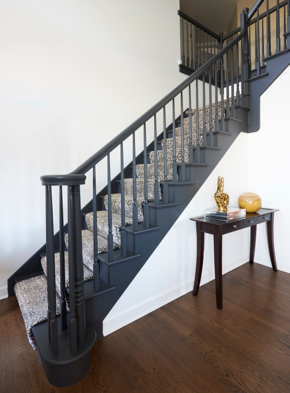Staircase painted fully in charcoal with turned balusters and a grey patterned runner beside a dark console table, by Martire Custom Homes