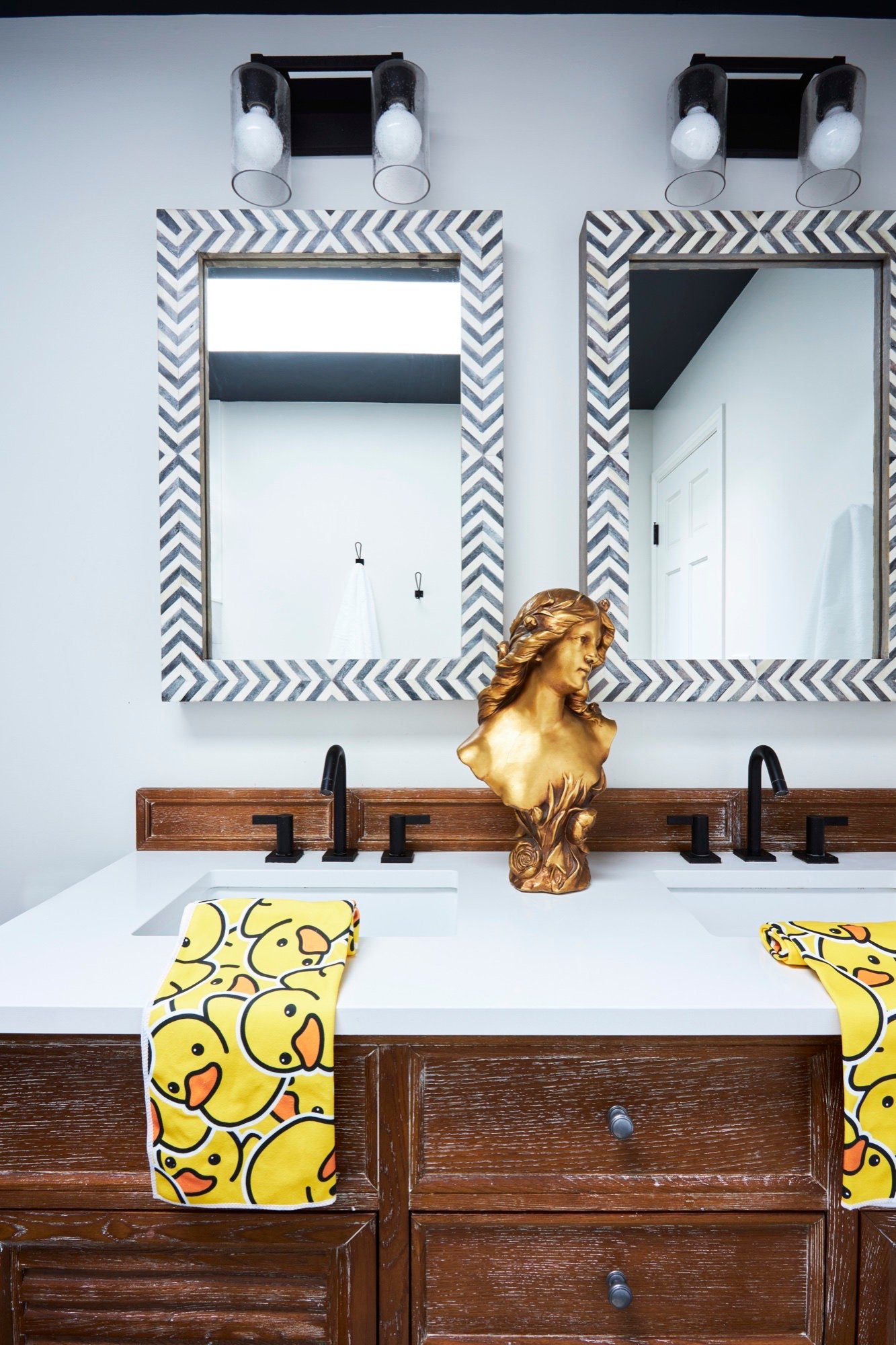 Children's bathroom double vanity with chevron bone-inlay mirrors, matte black faucets, white quartz top and cerused oak cabinetry, by Martire Custom Homes