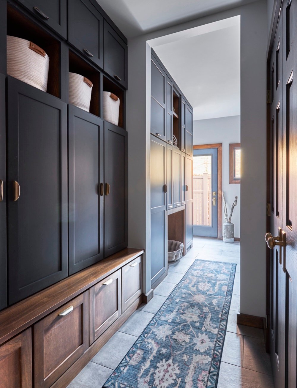 Mudroom with charcoal lockers over walnut bench drawers, blue runner and built-in dog bed nook, looking toward the laundry room door, by Martire Custom Homes