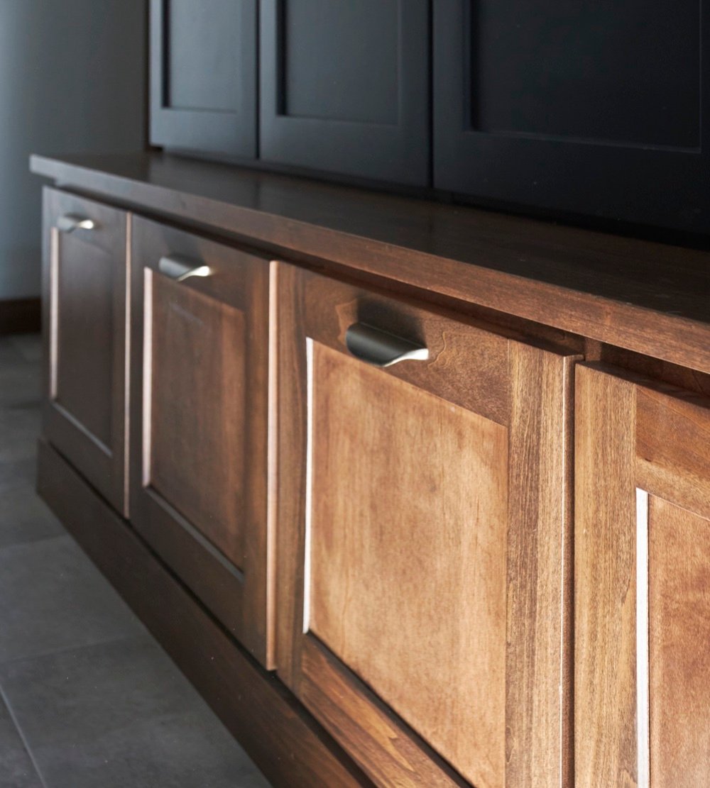 Close detail of walnut mudroom bench drawers with champagne bronze pulls beneath charcoal locker doors, by Martire Custom Homes