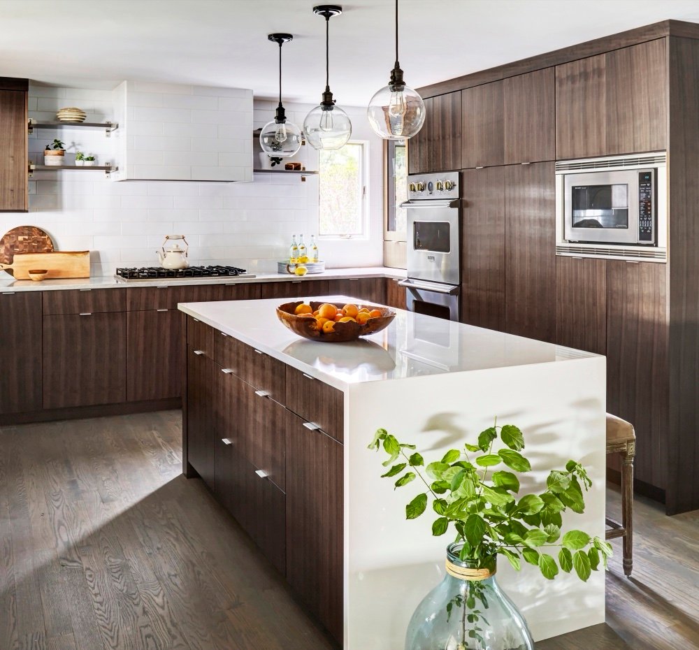 Kitchen with floor-to-ceiling rift-cut walnut cabinetry, a white quartz waterfall island and clear glass globe pendants over grey-washed hardwood, by Martire Custom Homes